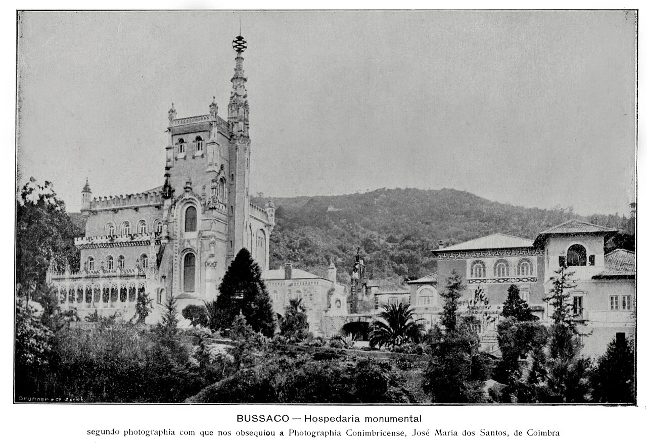 Black-and-white photograph from around 1900 of the Buçaco palace, its neo-Manueline tower rising above gardens with the forested ridge behind